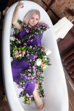 beautiful girl in lilac dress lies in bath with flowers in photo studioの写真素材