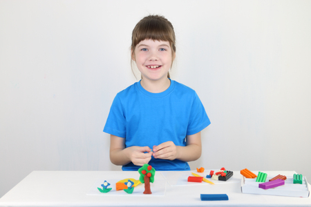 Happy girl in blue molds from plasticine on white table in white roomの写真素材