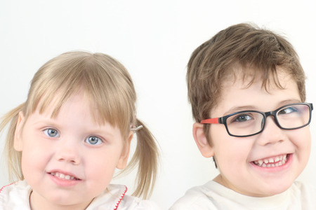Happy little blonde girl and boy in glasses smiles in white studioの写真素材