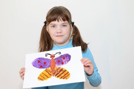 Girl shows picture with butterfly after watercolor painting in white roomの写真素材