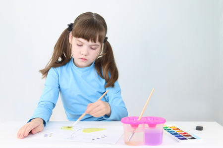Pretty girl in blue watercolor paints butterfly on table in white roomの写真素材