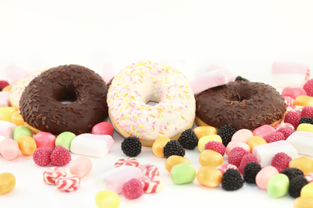 Sweet donuts, many bright candies and marshmallows on white tableの写真素材