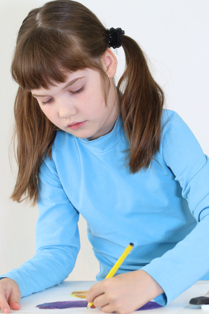 Happy girl paints watercolor butterfly with pencil on table in white roomの写真素材