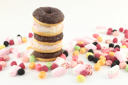 Five donuts, many bright candies and marshmallows on white surfaceの写真素材