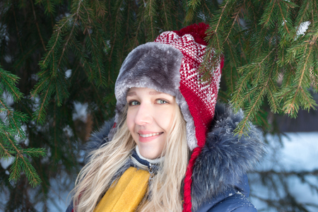 Young woman in hat stands near green fir tree outdoor in winterの写真素材