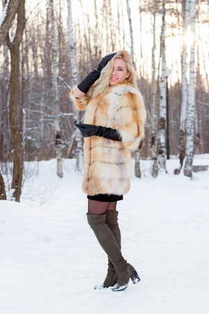 Pretty blonde in fur coat, leather gloves poses outdoor at winter day in forestの写真素材