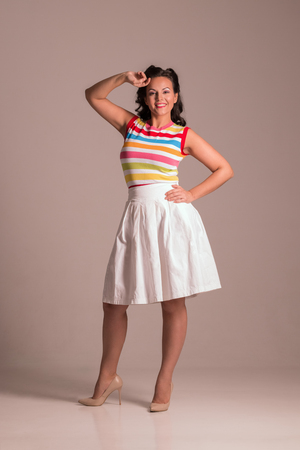 Beautiful woman in skirt with hairdo poses in grey studio, pin up style, full bodyの写真素材
