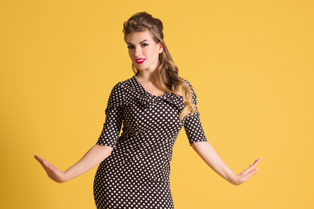 Pretty young woman in retro dress with hairdo stands in yellow studio, pin up styleの写真素材