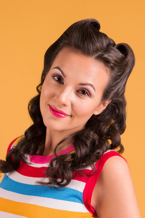 Young smiling woman in striped shirt, with hairdo stands in yellow studio, pin up styleの写真素材