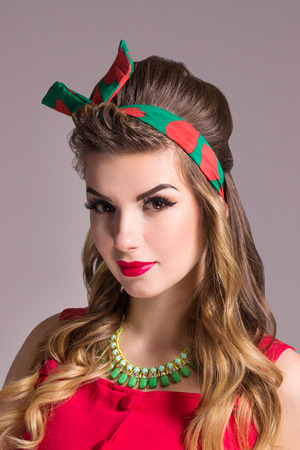 Woman in red dress with hairdo poses in grey studio, pin up styleの写真素材