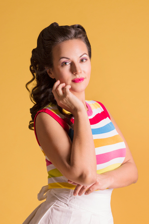 Young woman in striped shirt, with hairdo stands in yellow studio, pin up styleの写真素材