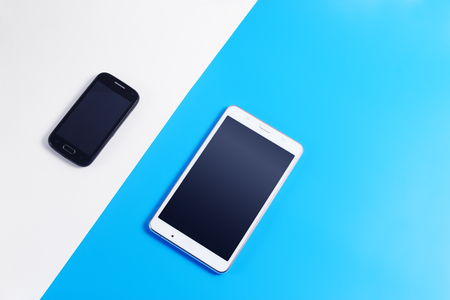 Black mobile phone and white tablet PC on white and blue background. top viewの写真素材
