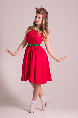 Beautiful woman in red dress with hairdo stands in grey studio, pin up styleの写真素材