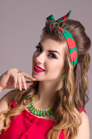 Smiling woman in red dress with hairdo poses in grey studio, pin up styleの写真素材