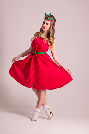 Pretty woman in red dress with hairdo stands in grey studio, pin up styleの写真素材