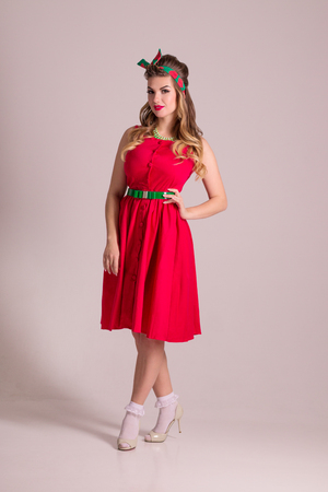 Pretty girl in red dress with hairdo stands in grey studio, pin up styleの写真素材