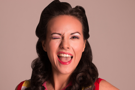 Pretty brunette with hairdo winking in studio, pin-up style, close-up portraitの写真素材