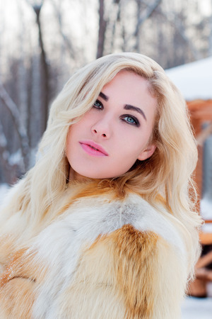 Beautiful blonde in fur coat poses in winter day in park, close upの写真素材