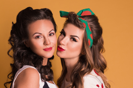 Two pretty women in dresses pose in orange studio, pin up styleの写真素材