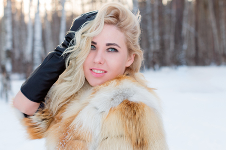Pretty young woman in fur coat poses outdoor at winter day in forestの写真素材