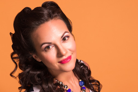 Happy brunette with hairdo and make up poses in studio, pin up style, close up portraitの写真素材