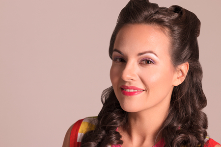 Pretty brunette with hairdo and make up smiles in studio, pin-up style, close-up portraitの写真素材