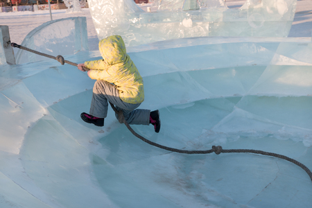 Happy girl in yellow warm clothes plays in big ice plate at winter sunny dayの写真素材