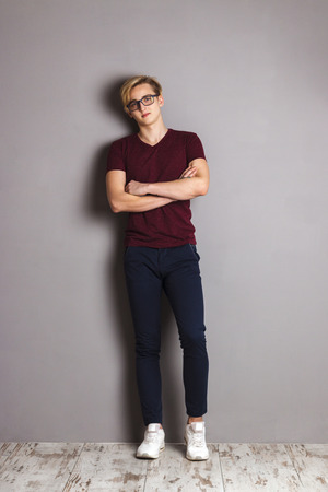 Handsome boy teenager stands with crossed arms near wall in grey studioの写真素材