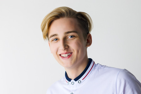 Handsome boy teenager in white shirt smiles in white studio, close upの写真素材