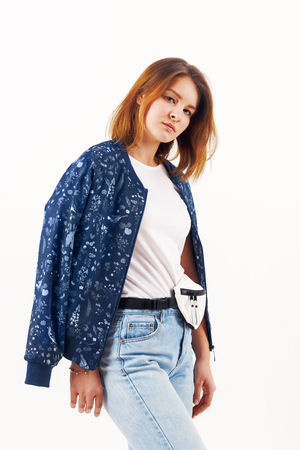 Pretty girl teenager in bomber and jeans poses in white studioの写真素材