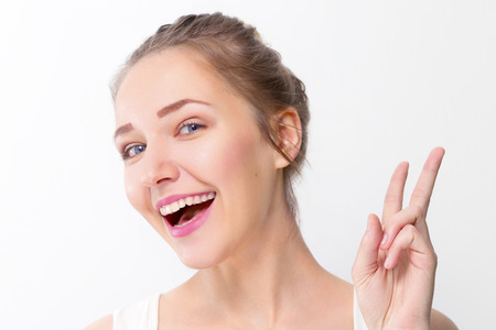 Pretty young girl with make-up shows peace gesture in studio, close up portraitの写真素材