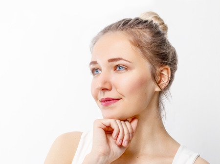 Pretty young girl with make-up props up chin and looks away in studio, close up portraitの写真素材