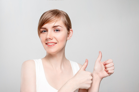 Beautiful young woman with make-up thumbs up and smiles in studioの写真素材