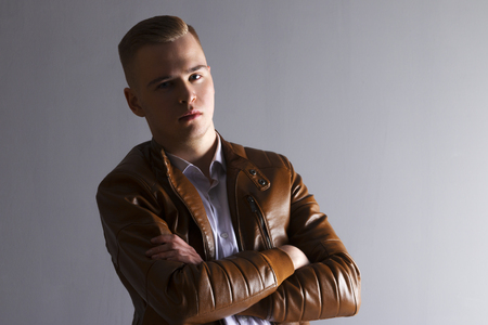 Handsome man in leather jacket poses with crossed arms in grey studioの写真素材