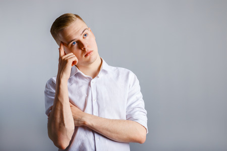 Young handsome man in white shirt touches hid head and thinks in studio