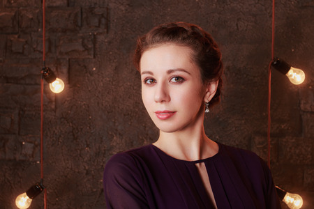 Pretty young woman stands in studio with brick wall and lampsの写真素材