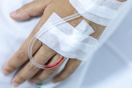 Close up hand woman patient with injection Saline in hand and during lying rehabilitation beds the hospital.の写真素材