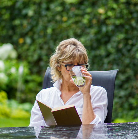 The modern woman reads a book in the garden after the rain and drinking water with lemonの写真素材