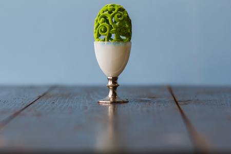 Easter decorative lacy green egg in a bronze egg cup on the blue background closeup on the table.の写真素材