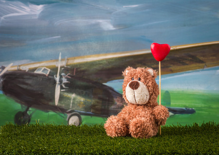 Valentine day concept. Teddy bear with heart is sitting on the grass near the aircraft.の写真素材