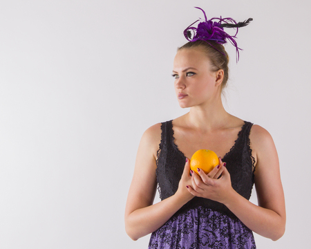 Mysterious unusual brunette woman in a smart purple lingerie holding in hands orange and looking thoughtfully into the distance.の写真素材