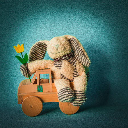 Teddy rabbit on theblue background sitting in a light on the  wooden car toy, quadrant combinationの写真素材