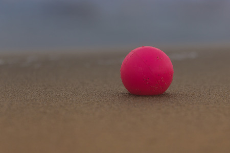 Close-up plastic pink ball lying in a sand of empty beach, horizontal.の写真素材