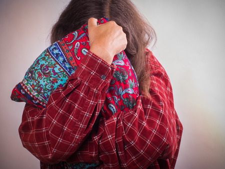 A woman with a red blouse and gray hair hid in a pillow. Woman issues concept.