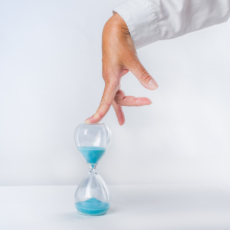 Hourglass with blue sand under the pressure of a finger of a woman. white background. Concept.