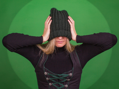 Young woman covers her face with a knitted hat and holds his head with his hands. Supression concept.の写真素材