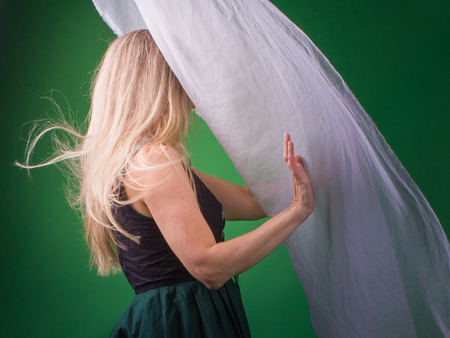Blonde woman withholds white silk against the lightの写真素材