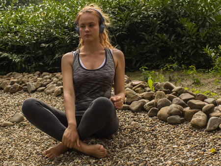 Young woman with a  long hair and headphones in Yoga pose-relaxed in garden with stone and plantsの写真素材