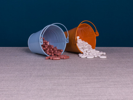 Pills in two pails on the table and dark blue background.