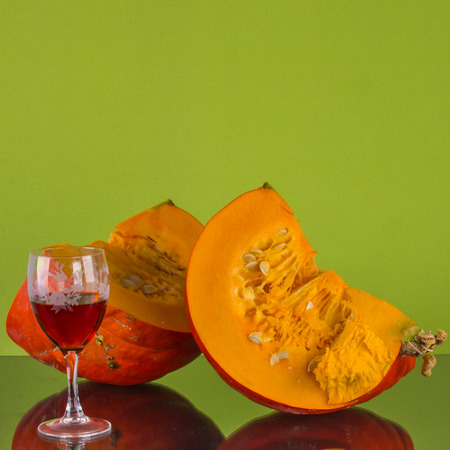Two half of pumpkin and glass of liquor on the pastel green background, close up.の写真素材